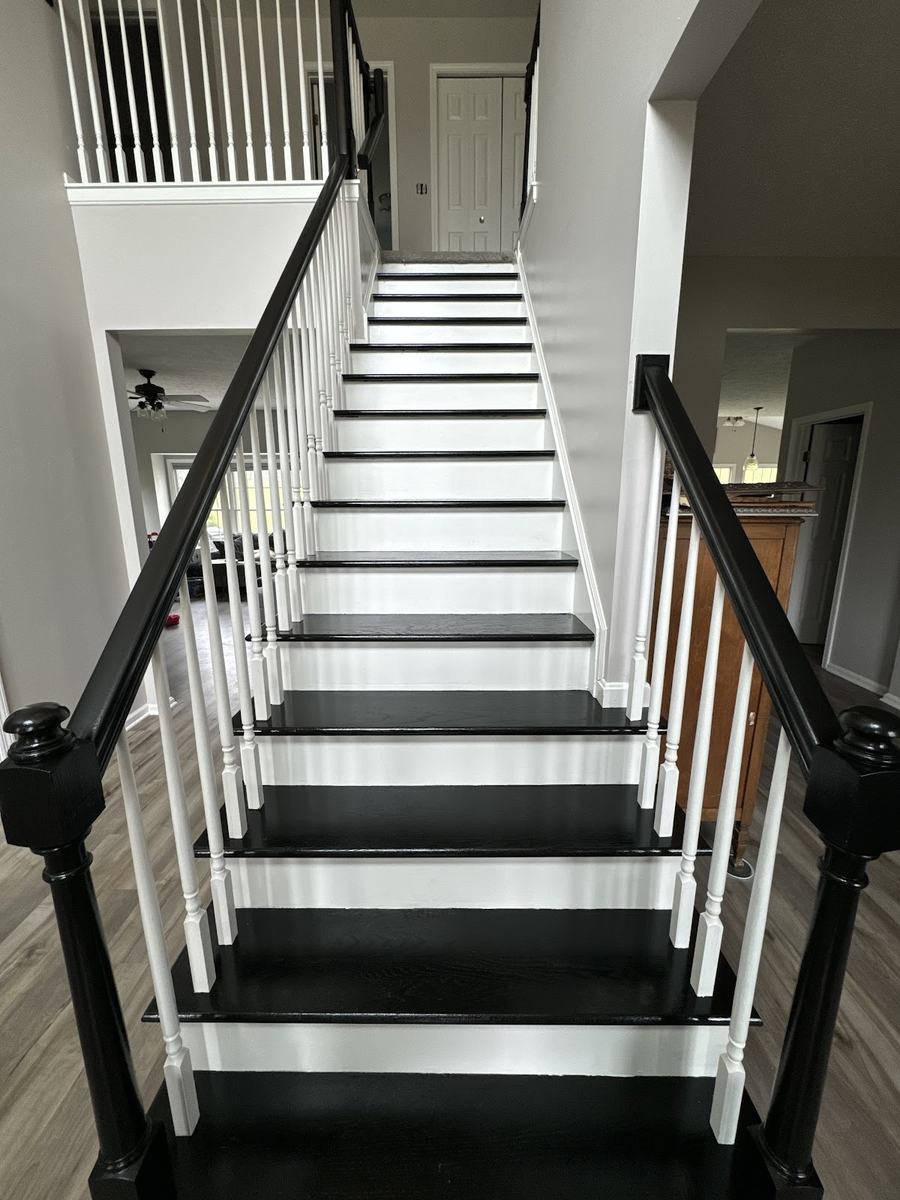 A staircase with white balusters and risers, black treads and a black newel and handrail.